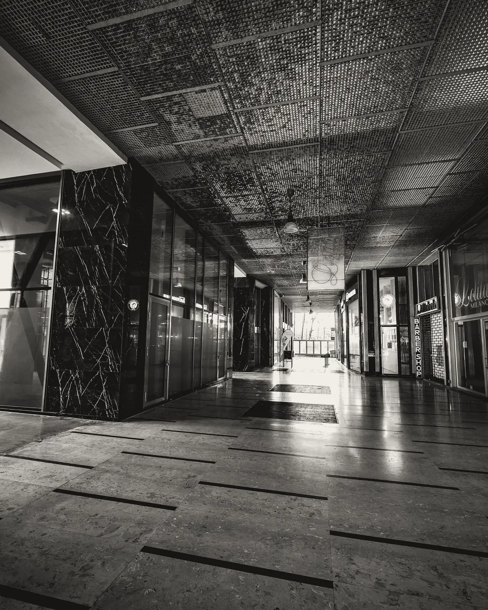 Black and white interior of spacious empty passage of building with glass doors and filing tiled walls