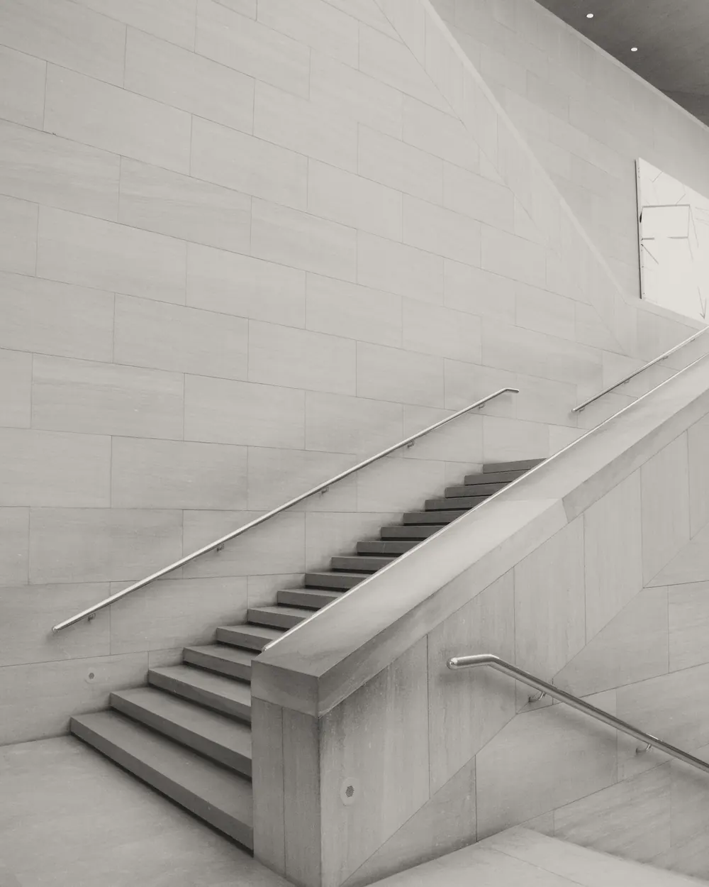 Black and white image of a minimalist modern staircase indoors with a single person ascending.